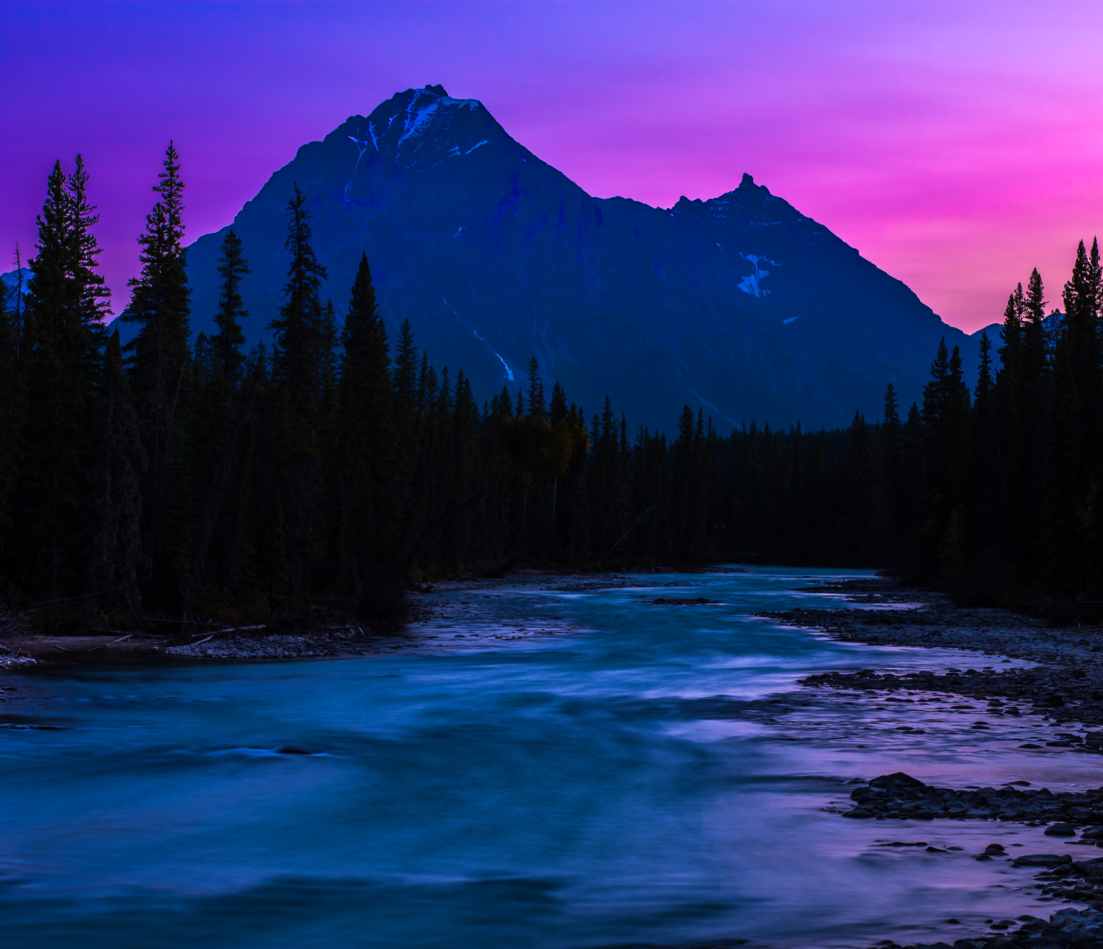 Sun setting behind the mountains with the last light filling the river blues hues as the night come-forth.