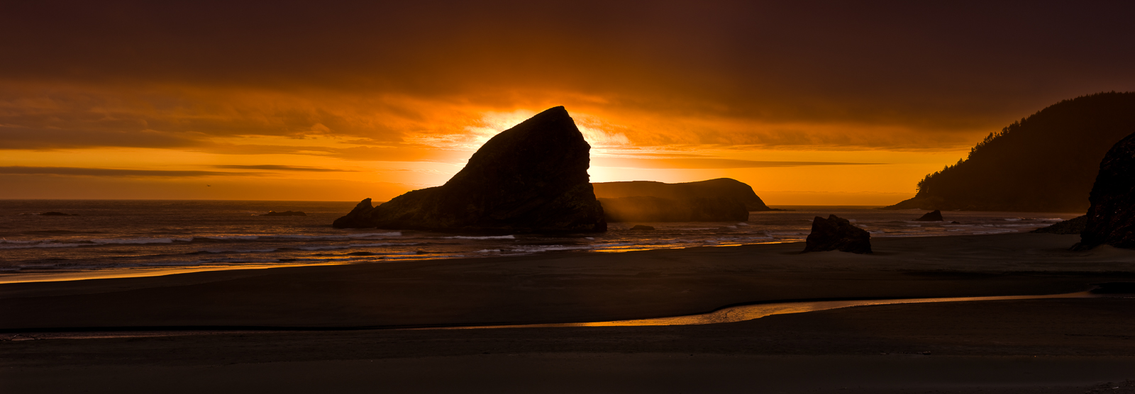 Setting sun halos around Maiden's Head Rock within the Pistol River State Park. The suns warm glow melts sea water into gold.